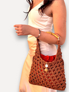 Borsa CapriNina EcoCapri all'uncinetto color marrone con manico in bambù indossata da una modella con abito bianco