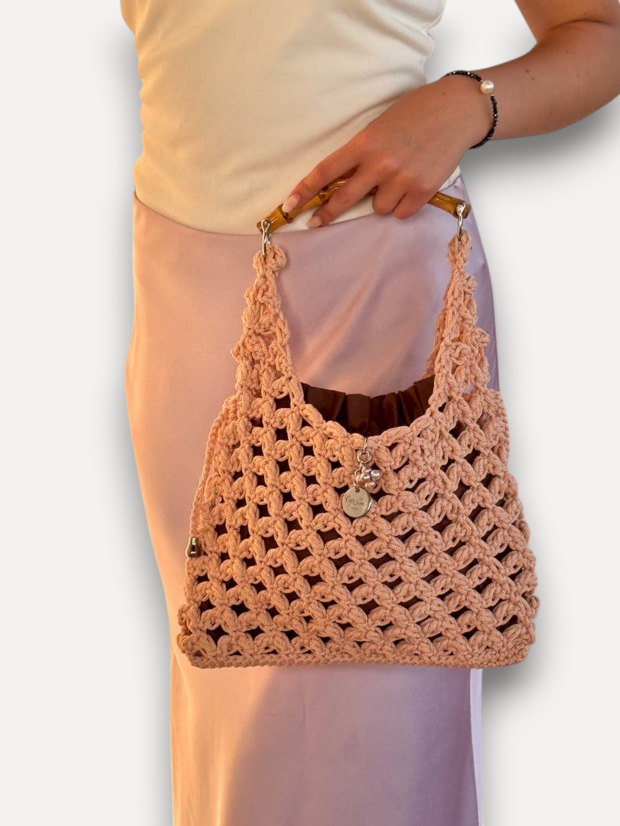 Borsa a mano CapriNina in crochet color pesca con manico in bambù e pochette interna, indossata con gonna satinata